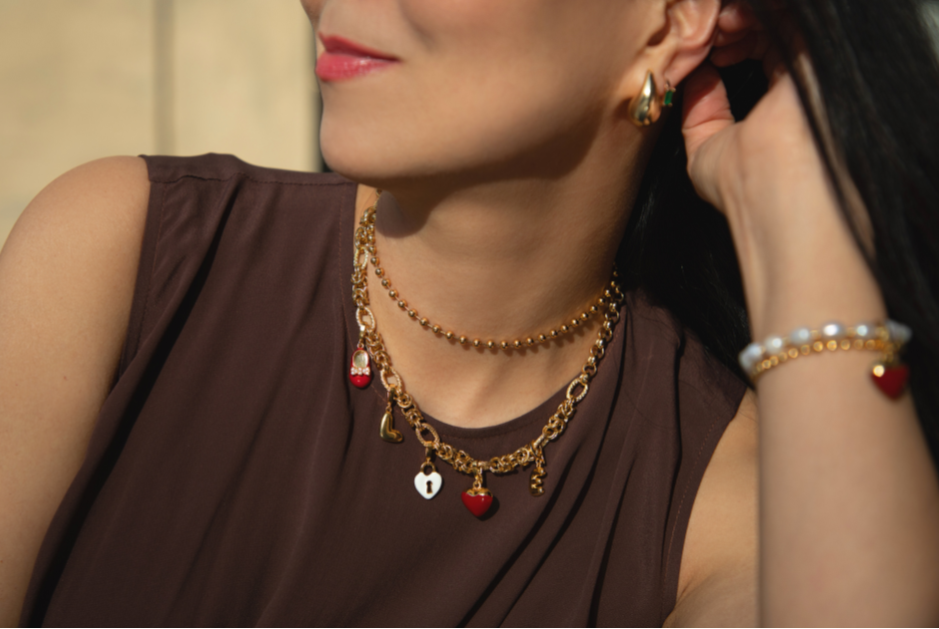 Woman wearing gold necklace, earrings, and bracelet with a neutral background